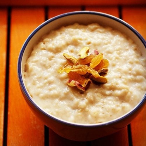 oats porridge garnished with chopped dry fruits and served in a blue rimmed white bowl.