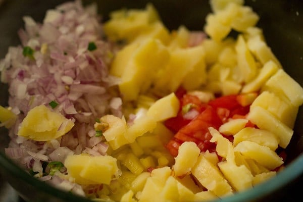 adding chopped boiled potato, chopped onion, chopped tomatoes and chopped green chilies to the chopped mango in the bowl. 