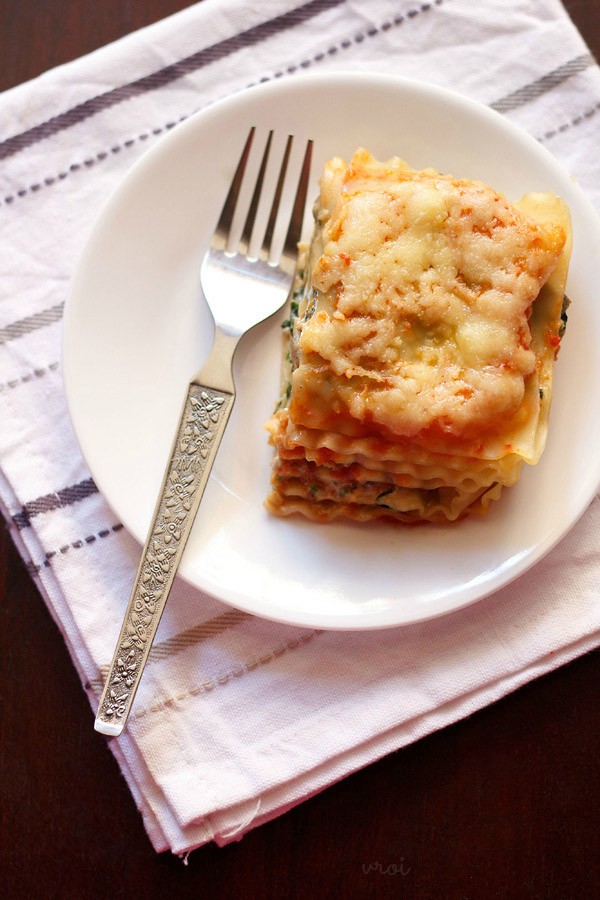 one slice of spinach mushroom lasagna on a white plate with a silver fork. 