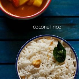 overheat shot of coconut rice topped with two fried curry leaves and cashew bits in a blue rimmed white bowl on a dark blue wooden tray