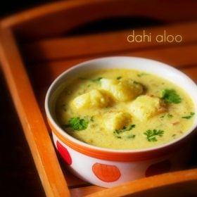 dahi wale aloo garnished with coriander leaves and served in a white with red dots ceramic bowl, kept on a wooden tray and text layover.