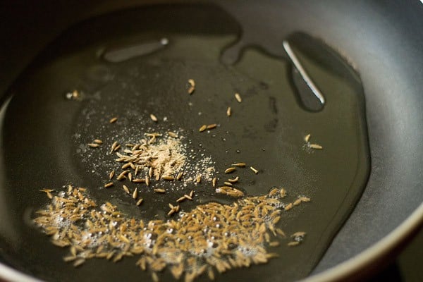 cumin seeds and asafoetida added to hot oil in pan. 