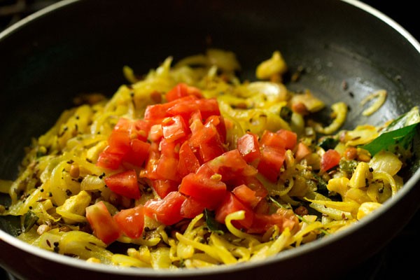 chopped tomatoes on a bed of cooked onions in pan.