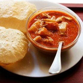 potato kurma served in a bowl with a spoon and pooris kept on a plate.