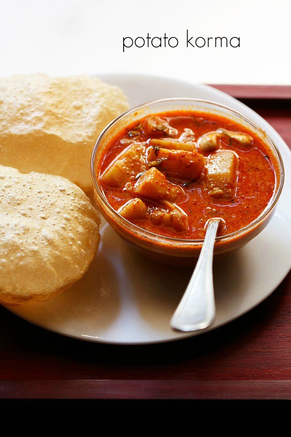 potato kurma served in a bowl with a spoon and pooris kept on a plate.