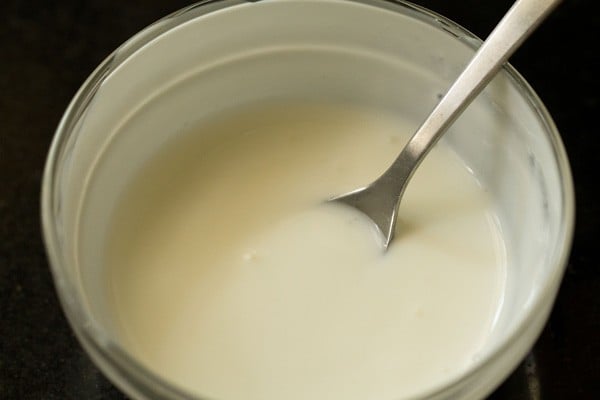 beating fresh full fat curd in a bowl with a spoon for aloo kurma. 