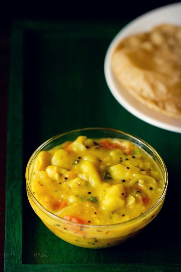 poori masala in a glass bowl with puri placed at the top.