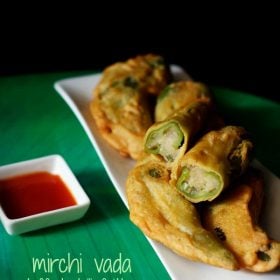 rajasthani mirchi vada served on a white platter with one halved vada on top, a bowl tomato sauce and text layovers.