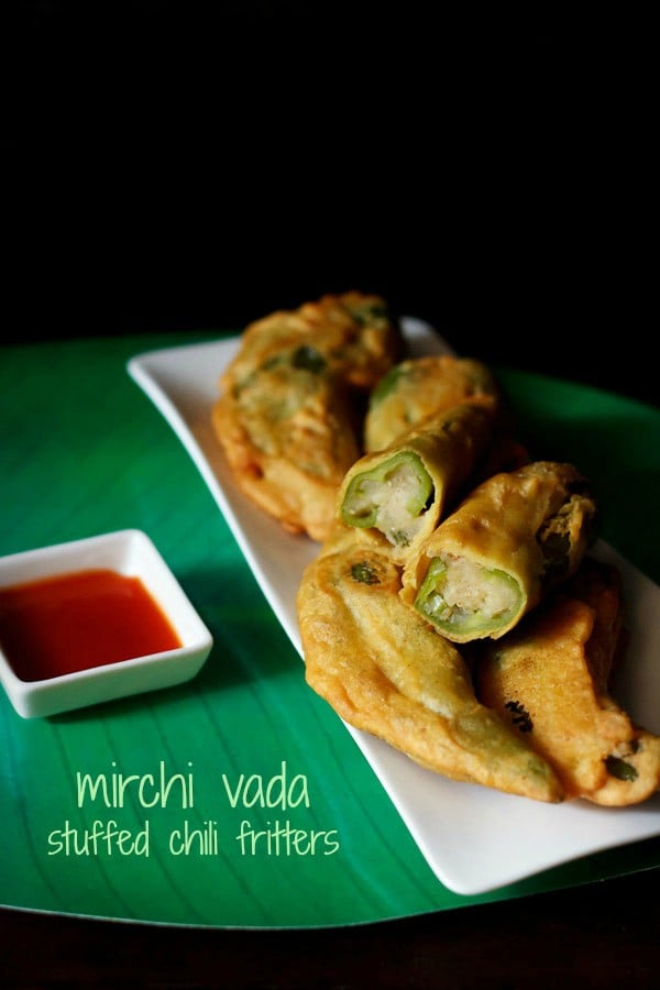 rajasthani mirchi vada served on a white platter with one halved vada on top, a bowl tomato sauce and text layovers.