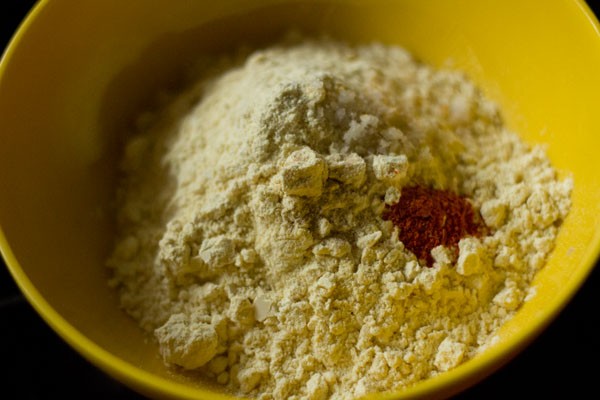 gram flour, red chili powder and asafoetida added in a bowl for making batter. 