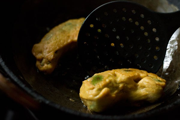 removing fried mirchi vada with a slotted spoon. 