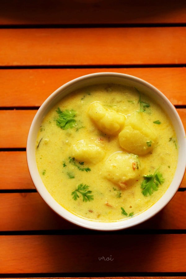 dahi wale aloo garnished with coriander leaves, served in a bowl and kept on a wooden tray. 