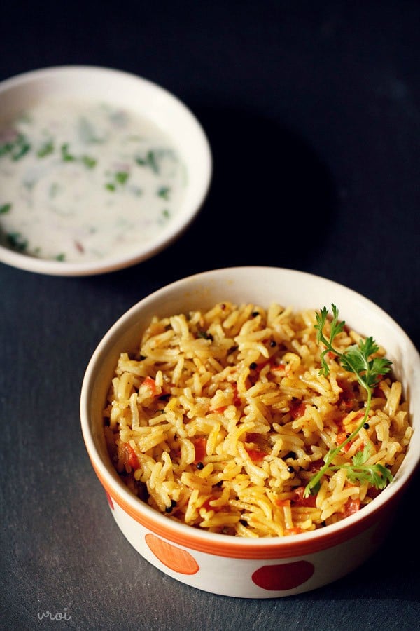 tomato rice served in an orange and red dotted bowl with a side yogurt raita on a dark black board