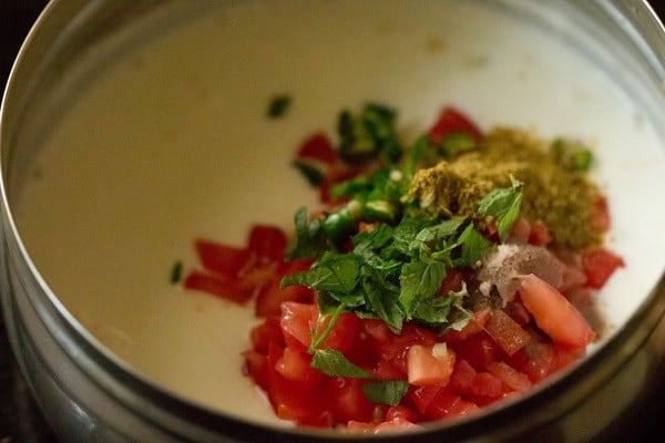 adding tomatoes, herbs and ground spices to whisked curd in a bowl