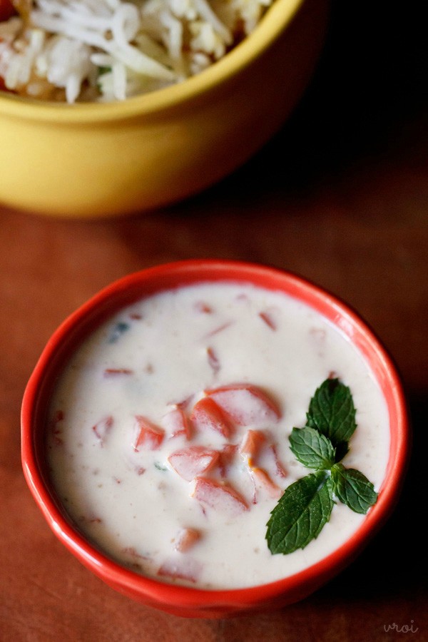 tomato raita served in a red bowl with mint leaf sprig for garnish