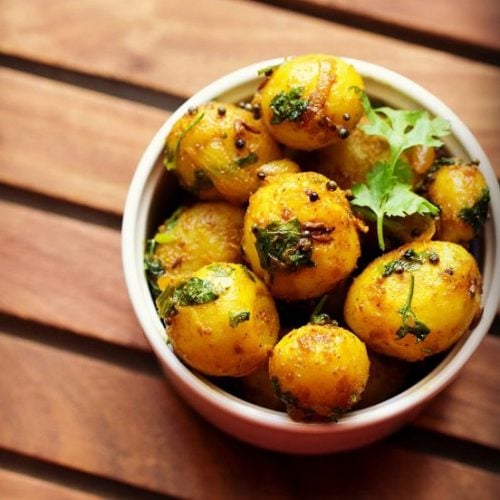 baby potato fry garnished with a coriander sprig and served in a white bowl.