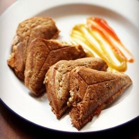 four capsicum sandwich triangles served on a white plate with tomato ketchup and chili sauce.