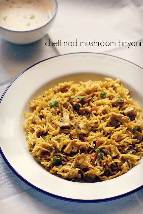 chettinad mushroom biryani in a blue rimmed white plate on a white table cltoh