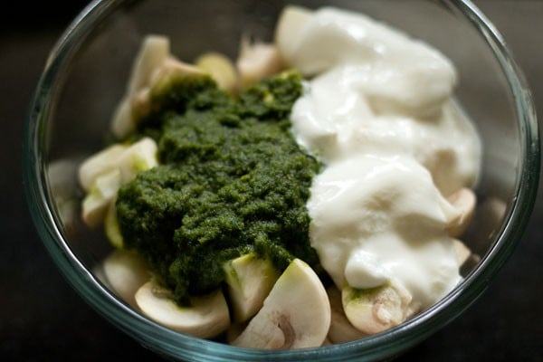 Ground green paste, curd, and chopped mushrooms in glass bowl.