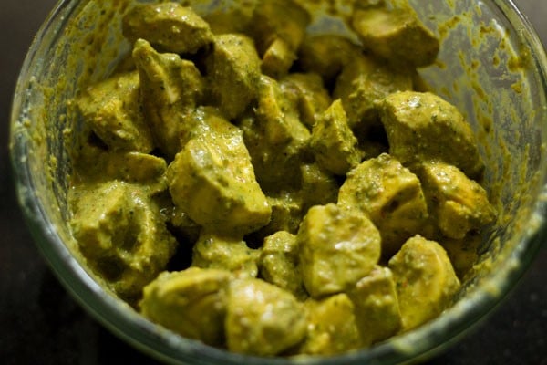 Mushrooms covered in green sauce in mixing bowl.