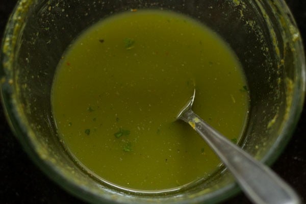 Water and green spice paste mix in mixing bowl with spoon.