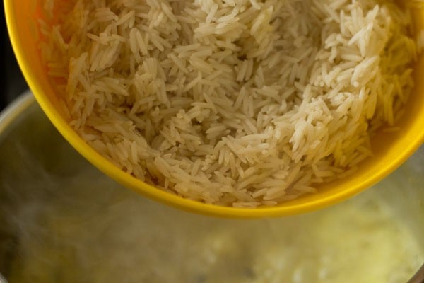 Rice in yellow bowl being added into gravy mixture.