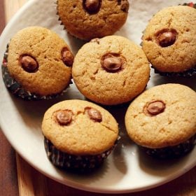 eggless chocolate chip muffins arranged neatly on a round plate placed on a bamboo board