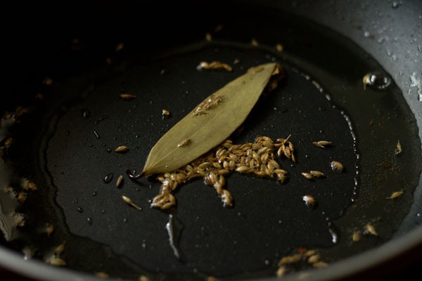 bay leaf and cumin seeds added to hot oil in pan. 