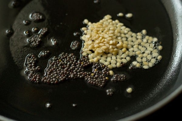 sautéing mustard seeds and urad dal in hot coconut oil in a pan for making raw banana sabzi. 