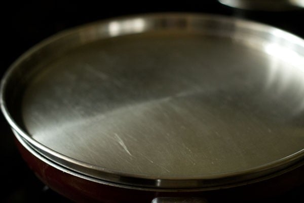 cooking raw banana poriyal in a pan covered with lid
