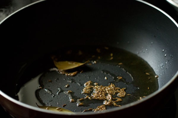 cumin seeds and bay leaves added to hot oil in pan. 