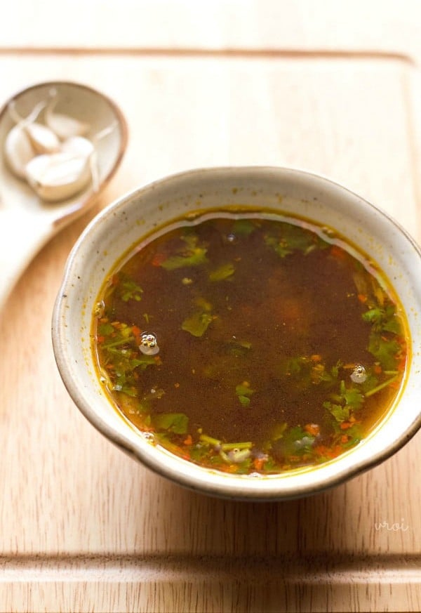 The garlic rasam is served in a white ceramic bowl. 