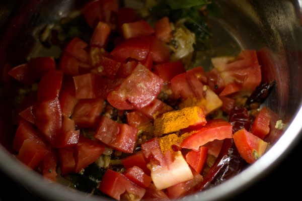 chopped tomato, turmeric powder and asafoetida added to pan for making garlic rasam. 