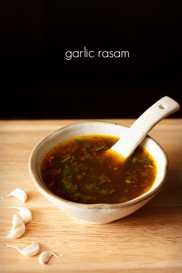 garlic rasam served in a white ceramic bowl with a spoon in it and text layover.