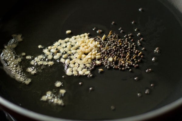 mustard seeds and urad dal added to hot sesame oil in pan. 