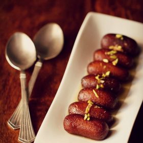 kala jamun served on a white platter with 2 spoons kept on the left side and text layover.