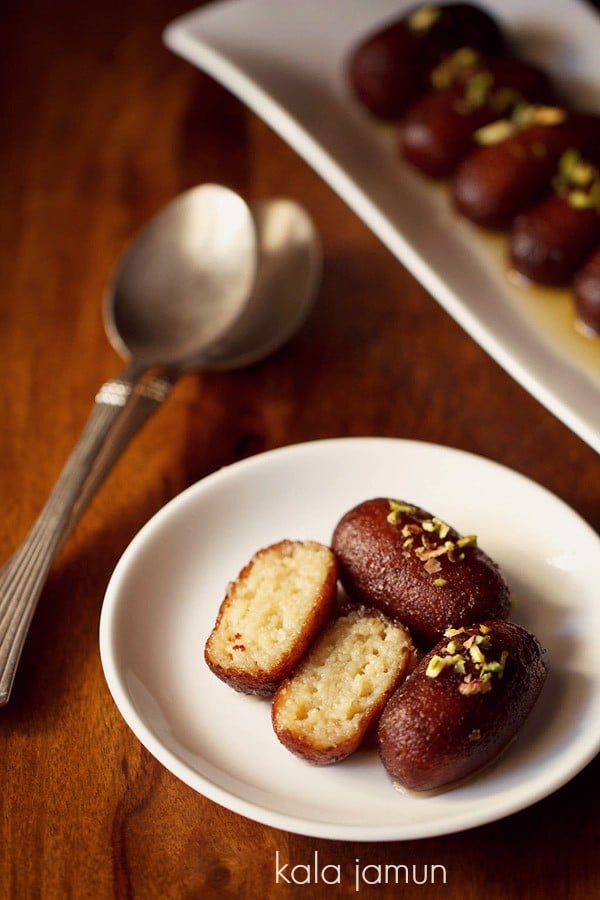 oblong serving platter of kala jamun and sugar syrup with a small round plate with 3 pieces of kala jamun on it and text layover.