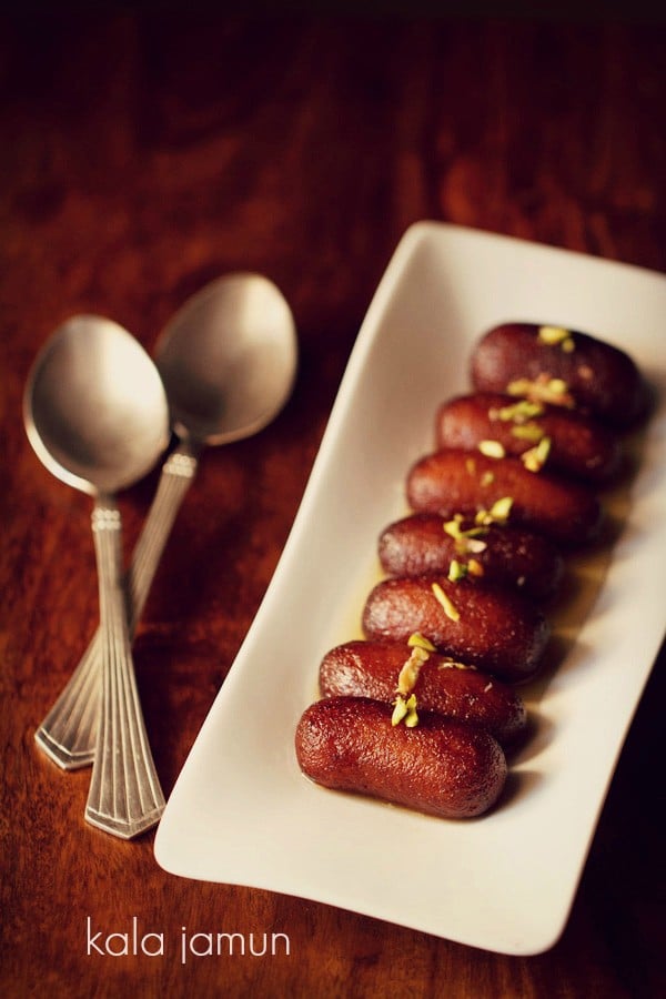 kala jamun served on a white platter with 2 spoons kept on the left side and text layover.