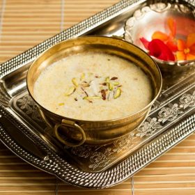 kaddu ki kheer in a decorative brass bowl on a silver tray with flowers in another bowl for offering to the Goddess.