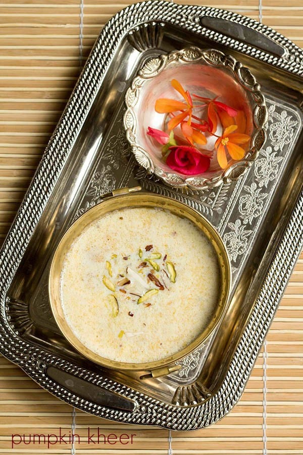 Overhead shot of pumpkin kheer (a.k.a. kaddu ki kheer or kaddu payasam) in a gold bowl on a silver tray with a silver bowl of flowers for offering to the goddess.