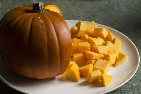 pumpkin on a white plate with part of it cut into cubes.