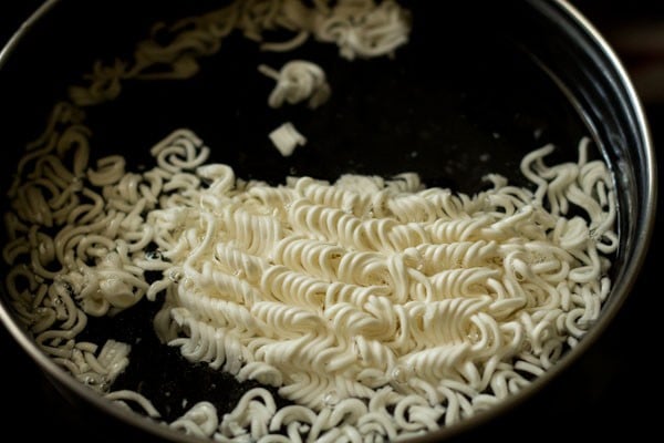 dried instant noodles added to water in pot