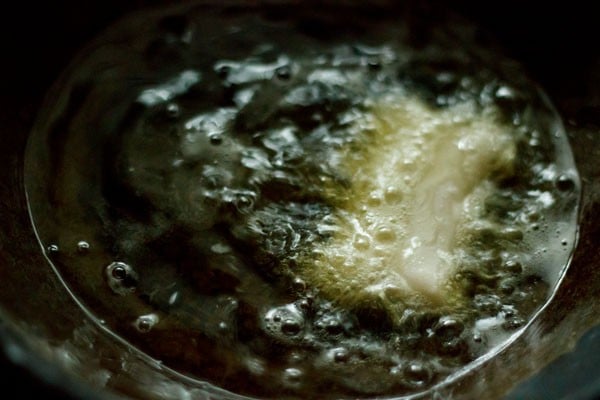 one vegetable spring roll frying in oil in a kadai