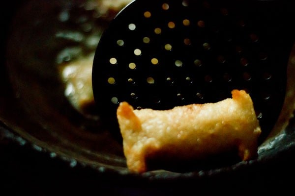 fried spring roll being removed from oil with a slotted spoon