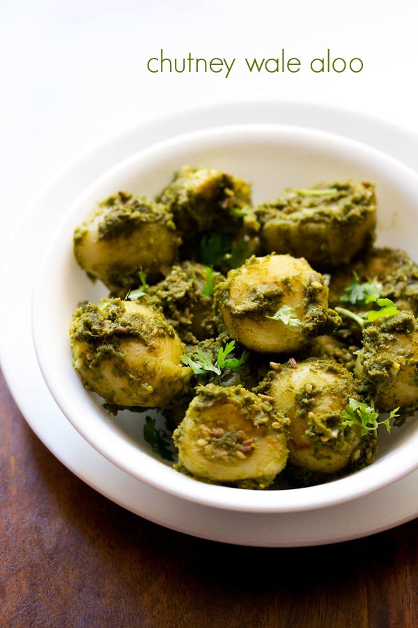chutney wale aloo adornado con hojas de cilantro y servido en un tazón blanco sobre un plato blanco con una escala de texto.