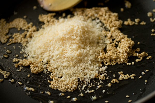 coconut added to pan with sesame seeds for dry fruits barfi recipe.