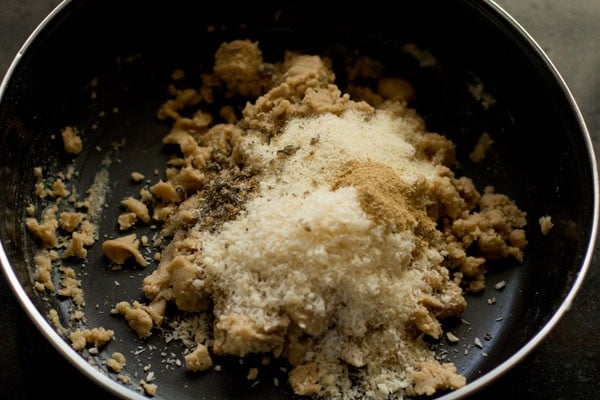 Kokosraspeln, Grieß, Kardamompulver und getrocknetes Ingwerpulver zu der Mehlmischung in der Schüssel geben. 