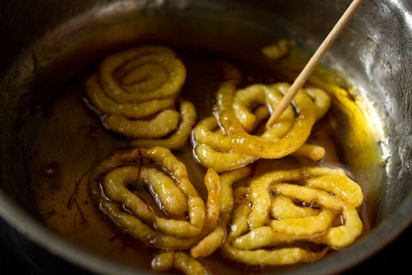 turning jalebi with a wooden skewer to coat with saffron sugar syrup