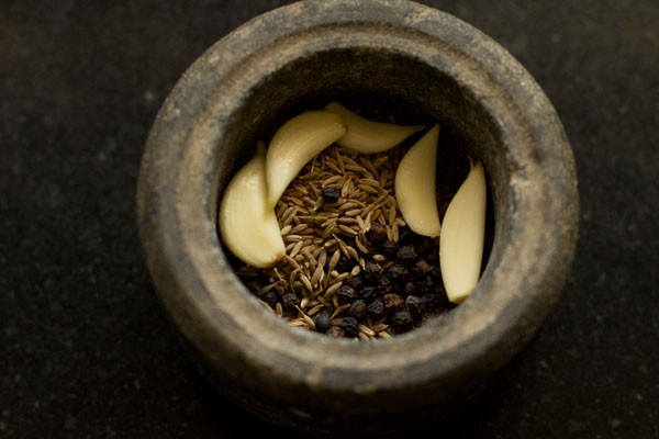cumin seeds, black pepper and garlic cloves in a mortar