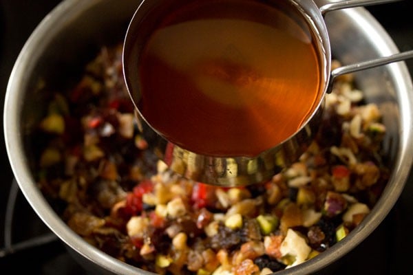 apple juice being added to chopped fruit and nuts for fruit cake recipe